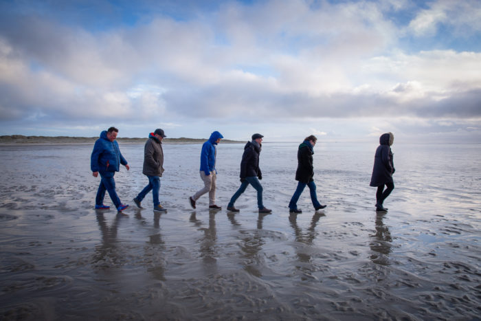 6 Menschen, hintereinander laufend am Strand/im Watt